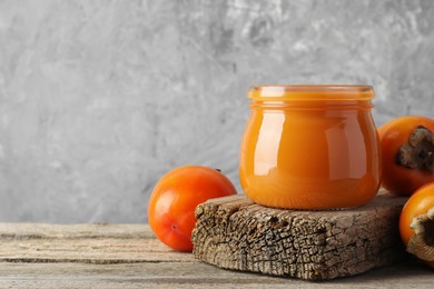 Delicious persimmon jam and fresh fruits on wooden table. Space for text