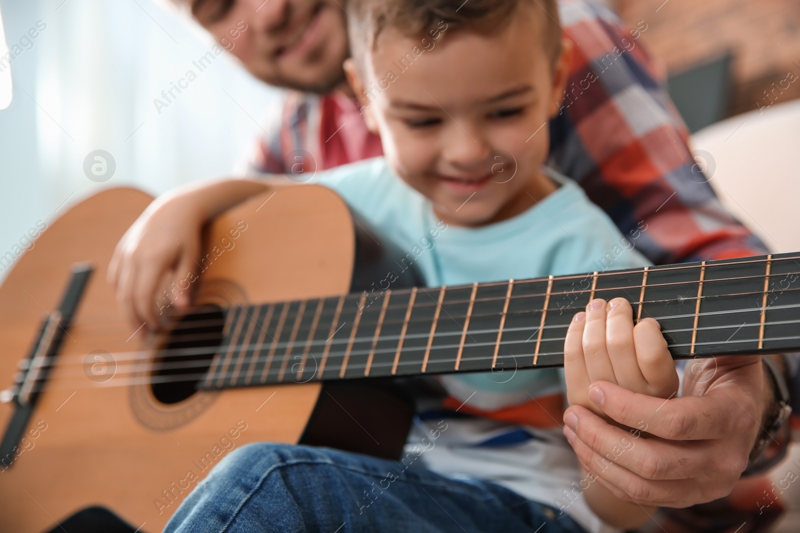 Photo of Father teaching his little son to play guitar at home