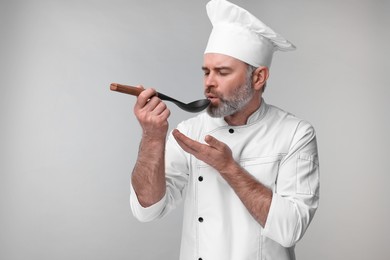 Chef in uniform tasting something on grey background