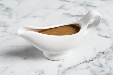 Photo of Delicious turkey gravy in sauce boat on white marble table