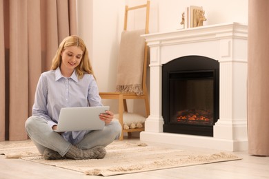 Young woman working on laptop near fireplace in room