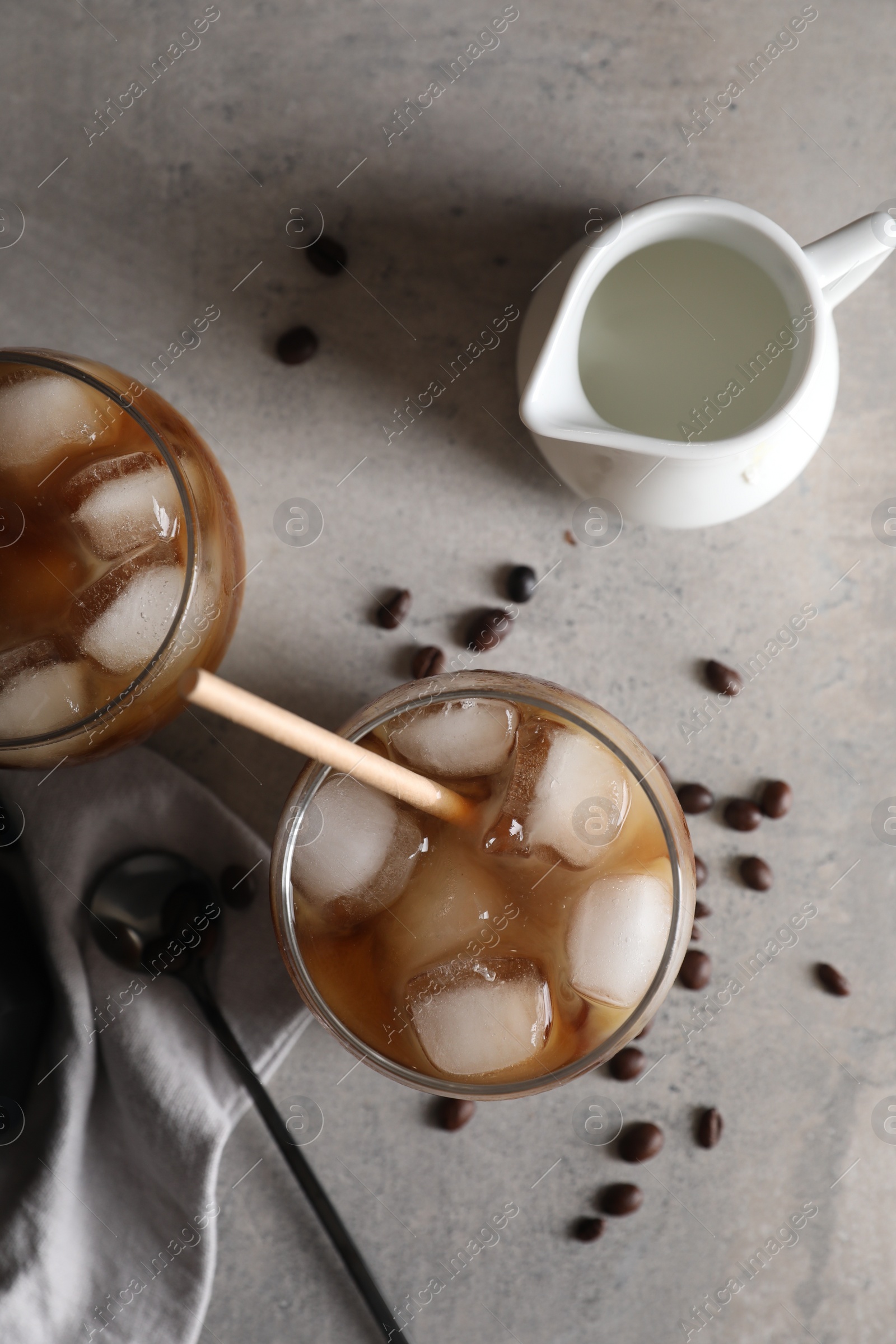 Photo of Refreshing iced coffee with milk in glasses, beans and spoon on gray table, flat lay