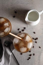 Refreshing iced coffee with milk in glasses, beans and spoon on gray table, flat lay