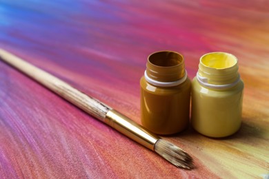 Photo of Jars with paints and brush on abstract picture, closeup