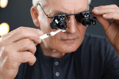 Photo of Male jeweler evaluating precious gemstone in workshop, closeup