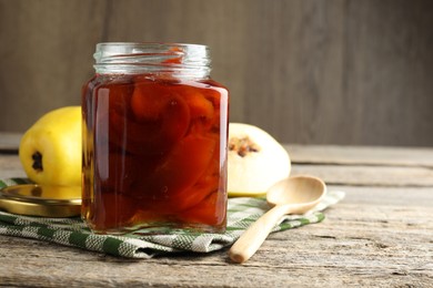 Tasty homemade quince jam in jar, spoon and fruits on wooden table, closeup. Space for text