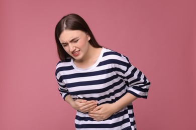 Photo of Young woman suffering from stomach pain on pink background