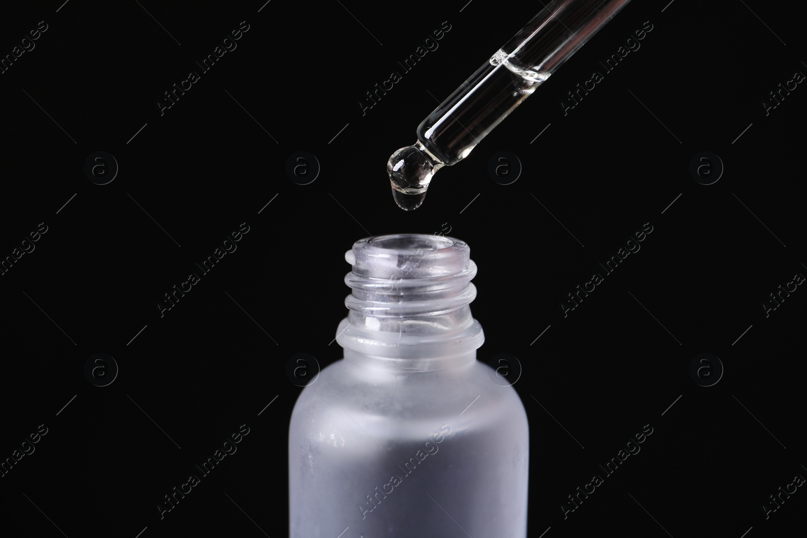 Photo of Dripping cosmetic serum from pipette into bottle on black background, closeup