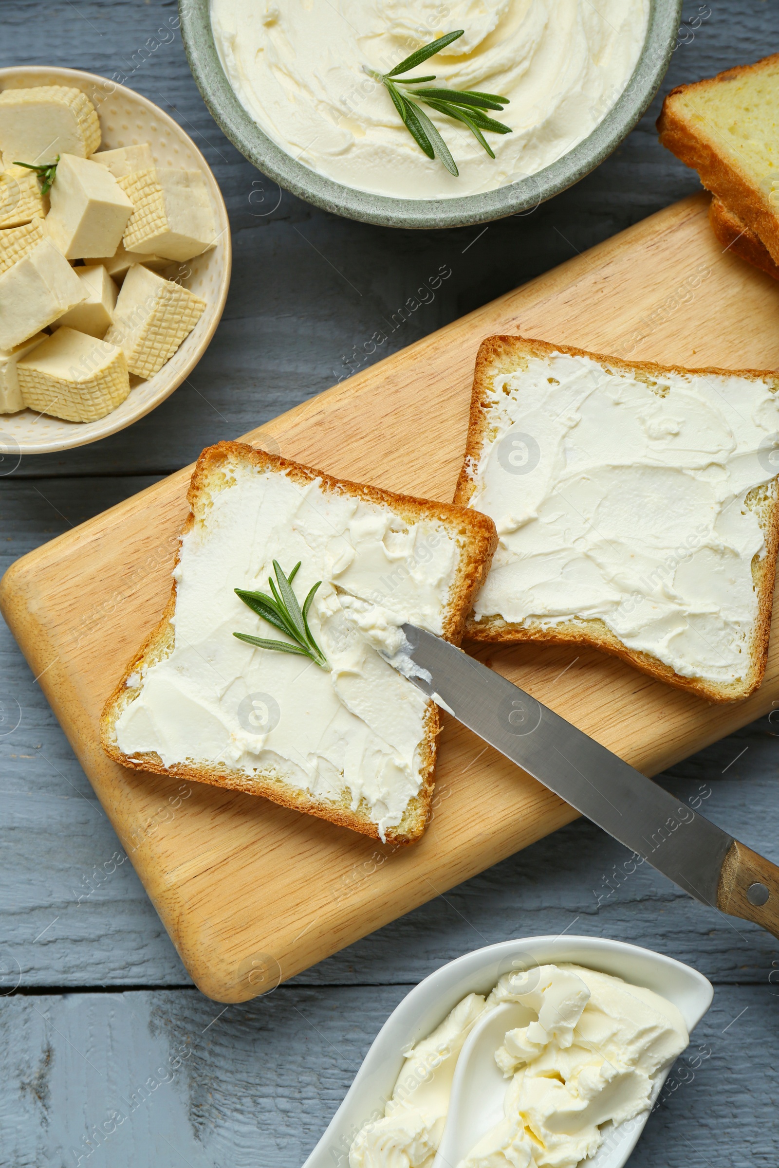 Photo of Delicious toasts with tofu cream cheese and rosemary on grey wooden table, flat lay