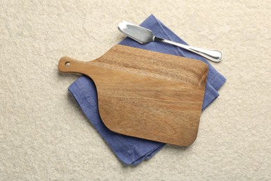 Wooden cutting board, napkin and butter knife on beige table, top view. Space for text