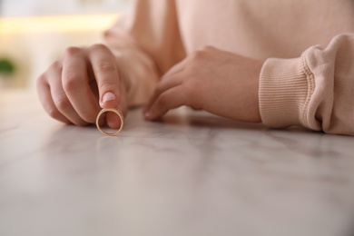 Woman holding wedding ring at table indoors, closeup. Divorce concept