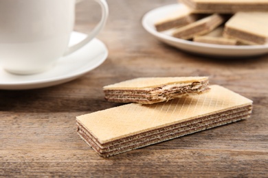 Photo of Delicious wafers and cup of drink on brown wooden background, closeup