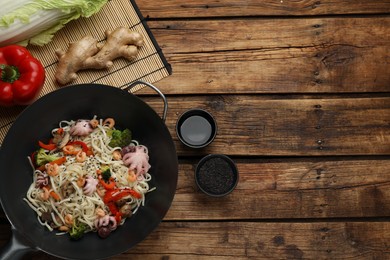 Stir fried noodles with seafood and vegetables in wok on wooden table, flat lay. Space for text