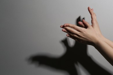Photo of Shadow puppet. Woman making hand gesture like bird on grey background, closeup. Space for text