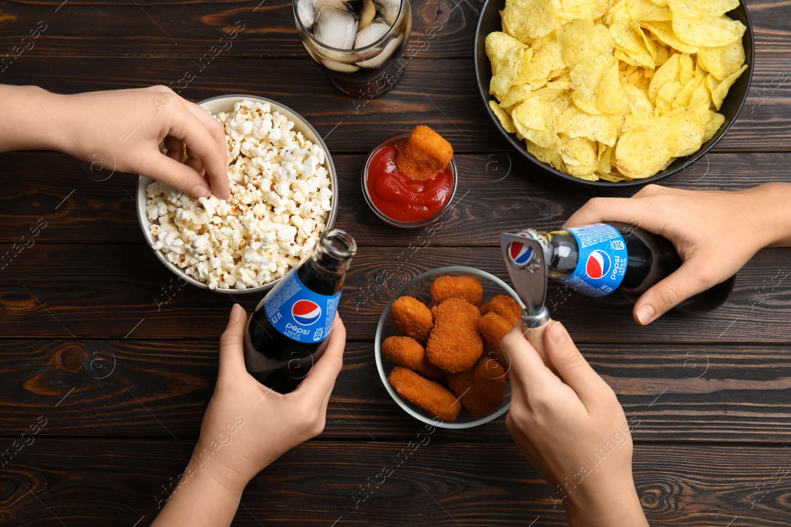 Photo of MYKOLAIV, UKRAINE - FEBRUARY 16, 2021: People with Pepsi and snacks at wooden table, top view