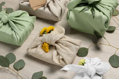 Photo of Furoshiki technique. Many gifts packed in fabric, flowers and eucalyptus leaves on wooden table