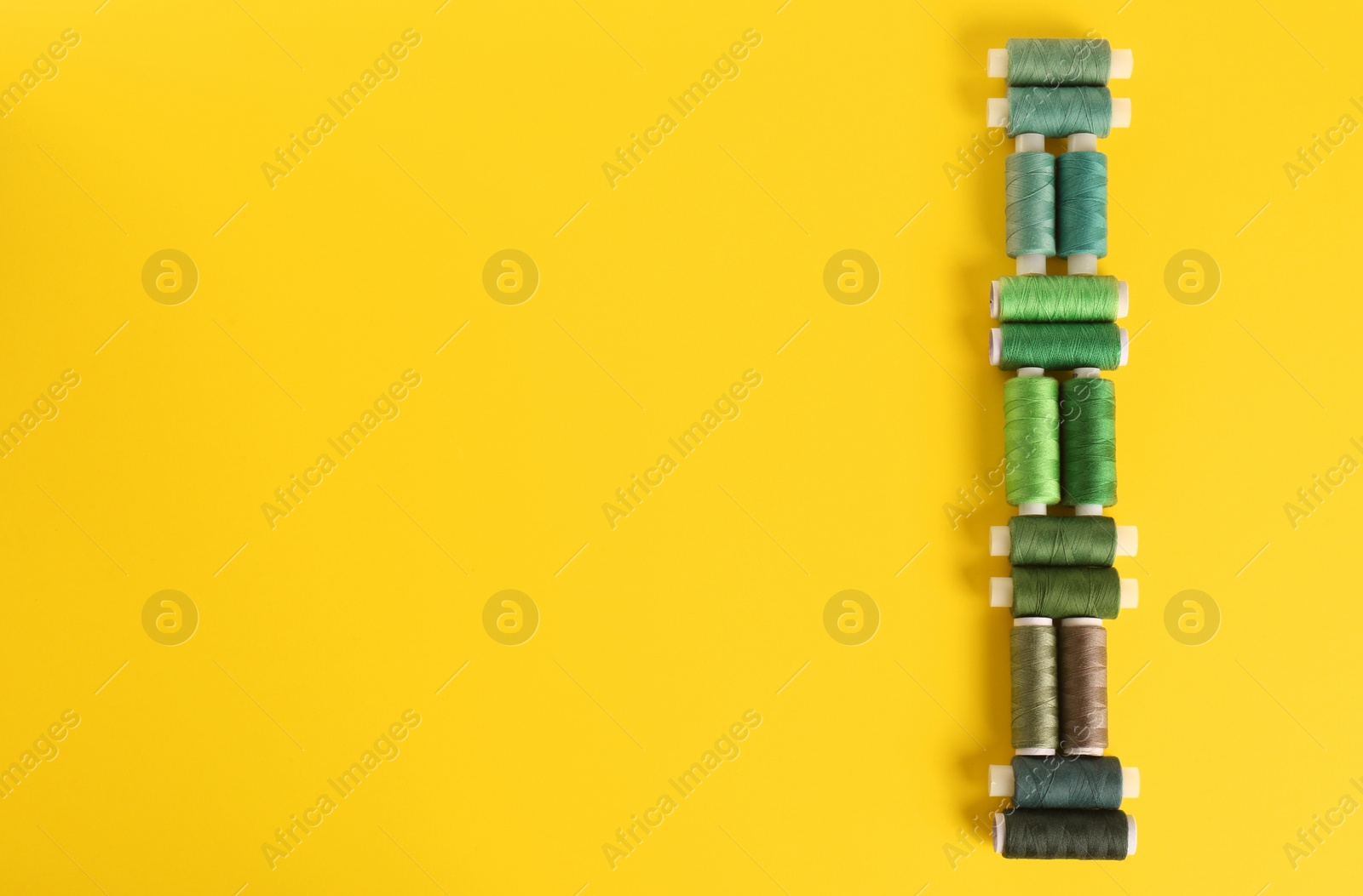 Photo of Different shades of green sewing threads on yellow background, flat lay. Space for text