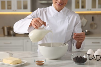 Professional chef adding milk into dough at white marble table indoors, closeup
