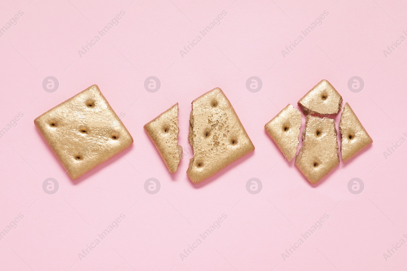 Photo of Golden whole and cracked cookies on light pink background, flat lay