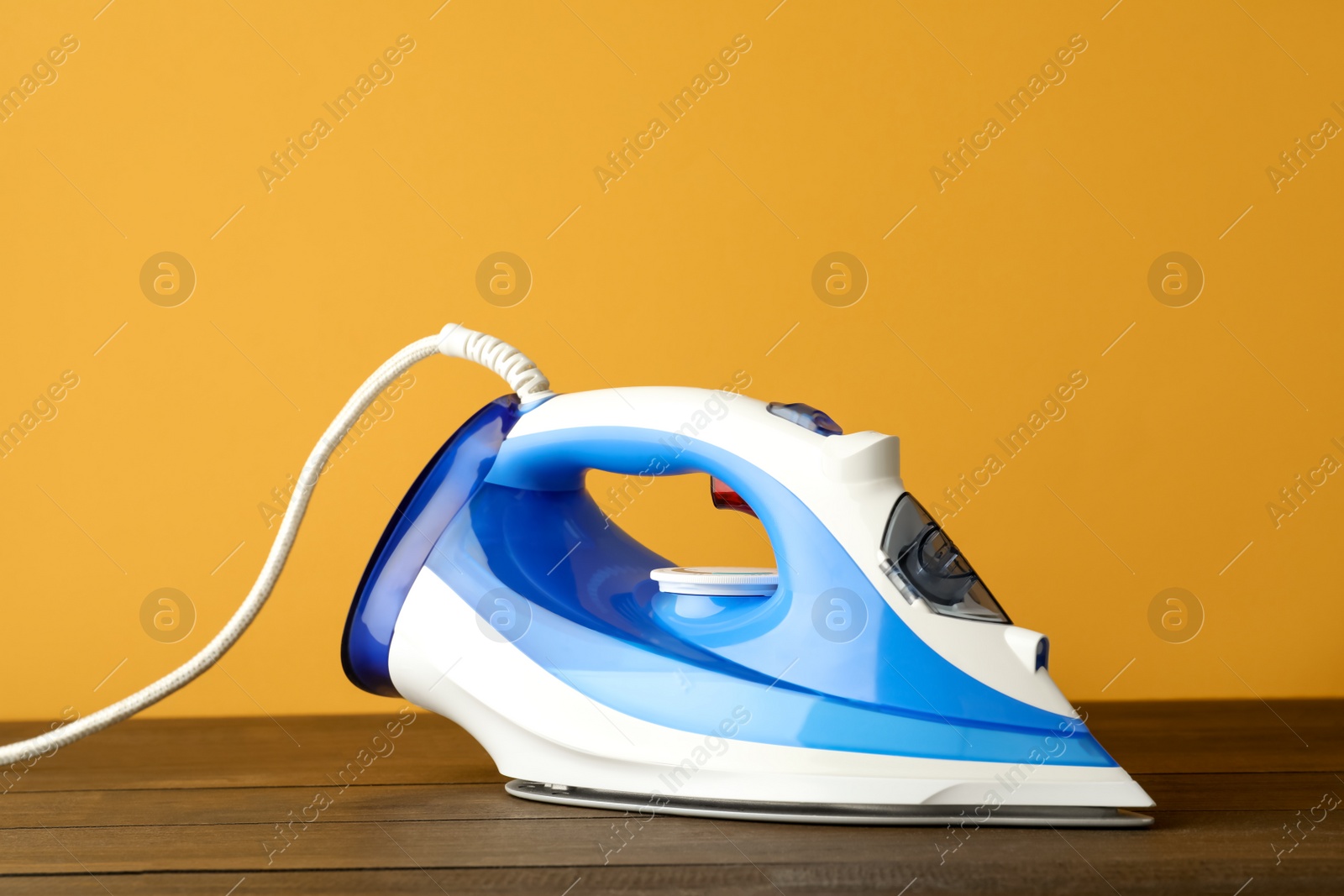 Photo of One modern iron on wooden table against orange background. Home appliance