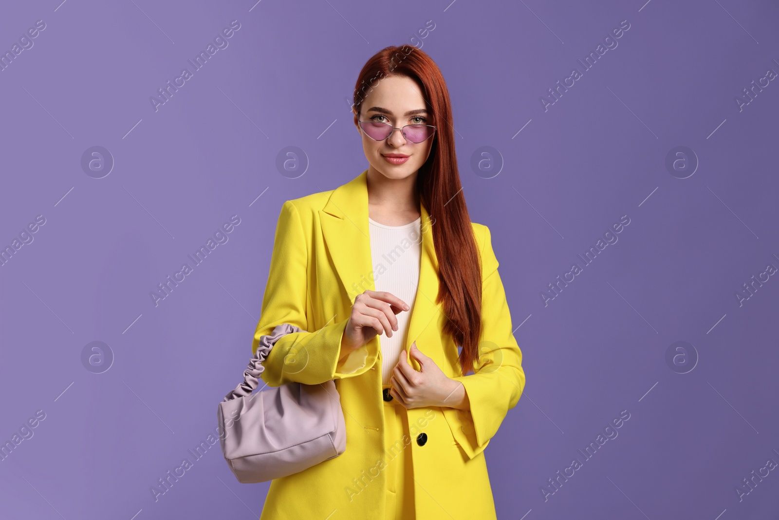 Photo of Stylish woman with red dyed hair and bag on purple background