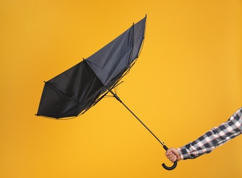Photo of Man holding umbrella caught in gust of wind on yellow background, closeup