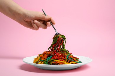 Photo of Woman eating delicious spaghetti painted with different food colorings on pink background, closeup