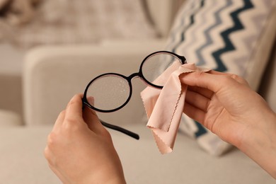 Photo of Woman cleaning glasses with microfiber cloth at home, closeup