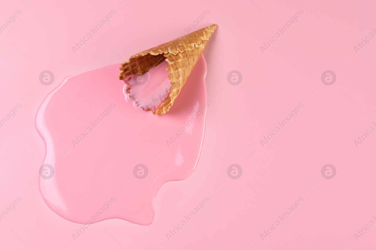 Photo of Melted ice cream and wafer cone on pink background, top view. Space for text