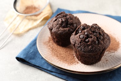 Delicious chocolate muffins and cacao powder on light grey table, closeup. Space for text