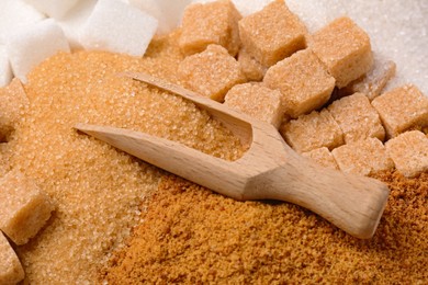 Scoop and different types of sugar as background, closeup