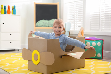 Photo of Little child playing with plane made of cardboard box at home