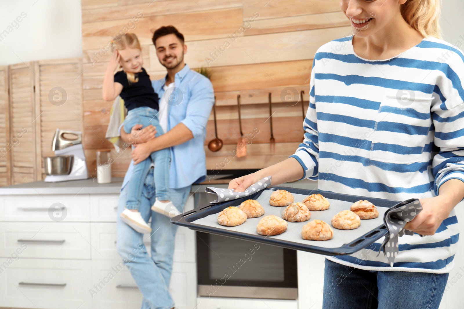 Photo of Young woman treating her family with homemade oven baked cookies in kitchen