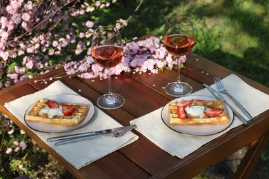 Delicious Belgian waffles with fresh strawberries and wine served on table in spring garden
