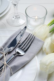 Photo of Stylish setting with cutlery, burning candle and tulips on white wooden table, closeup