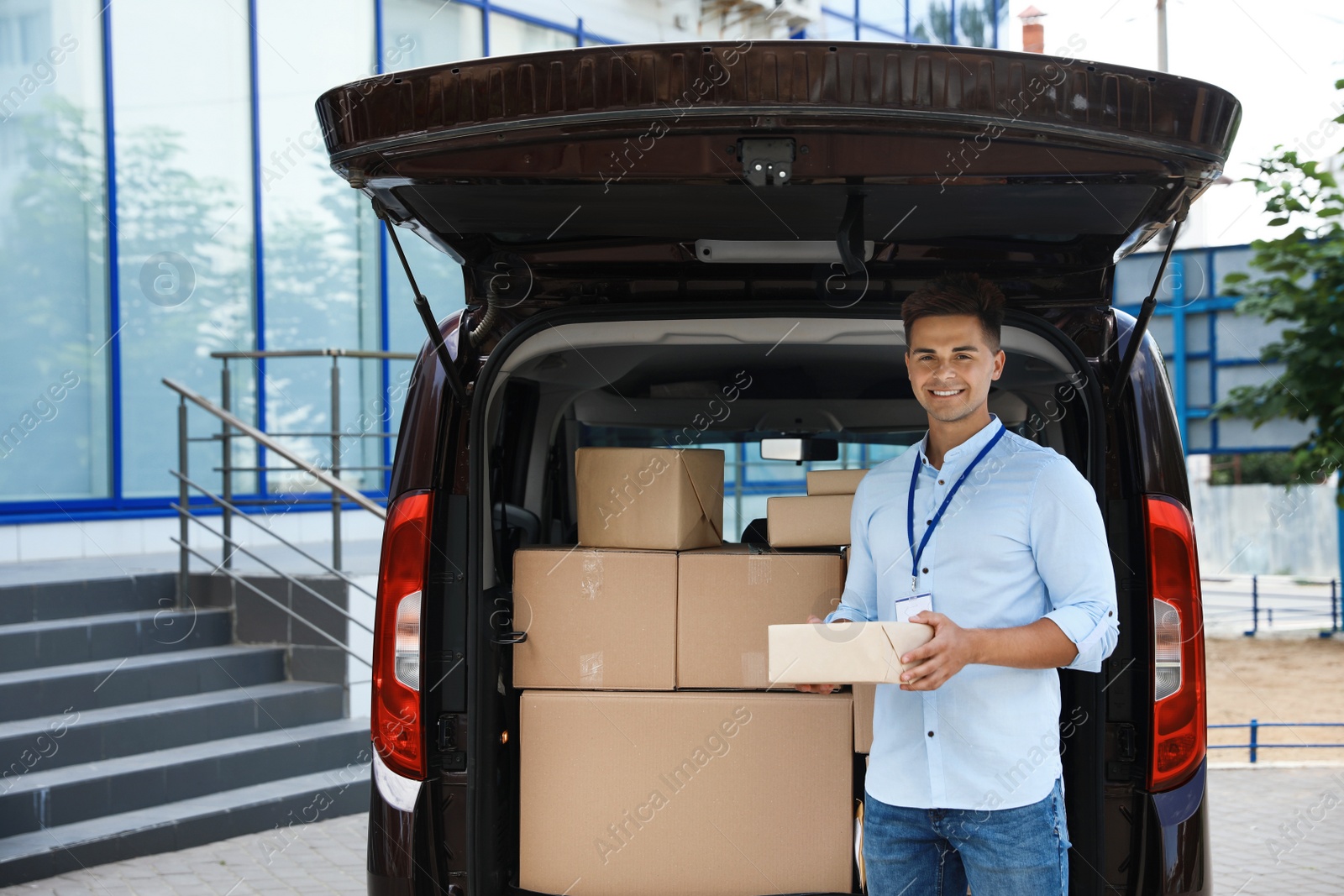 Photo of Young courier with parcel near delivery car outdoors