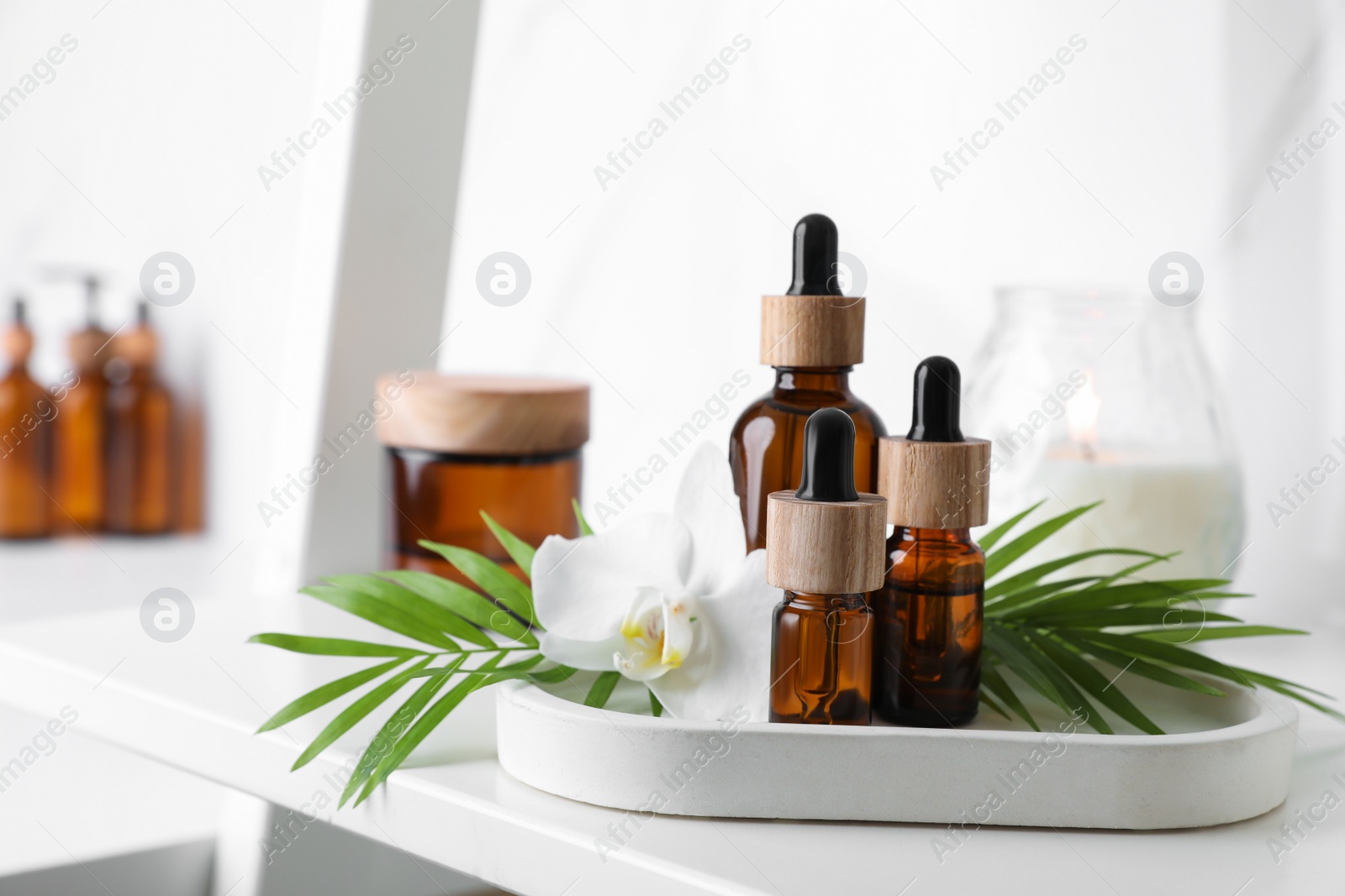 Photo of Essential oils, green leaves and orchid flower on white shelf in bathroom