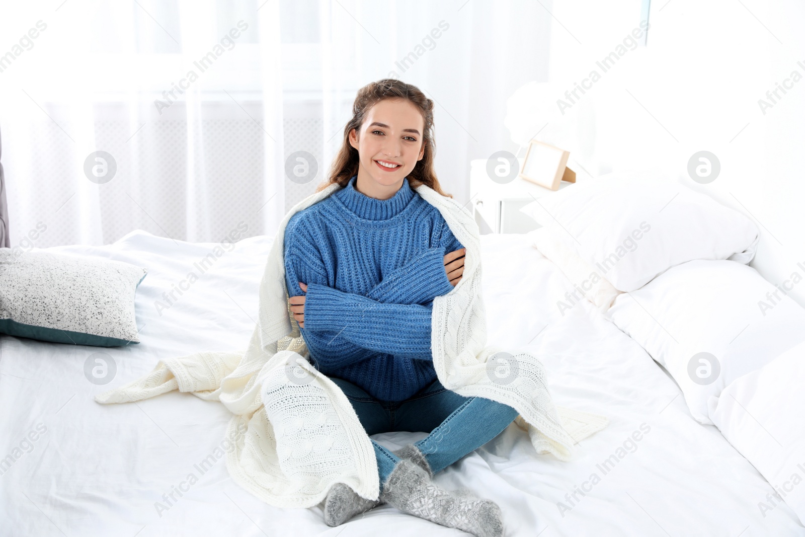 Photo of Beautiful teenage girl in warm cozy sweater with plaid sitting on bed at home