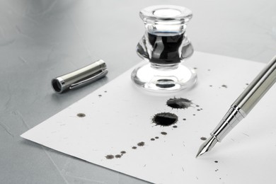 Stylish fountain pen, inkwell and paper with blots of ink on light grey textured table