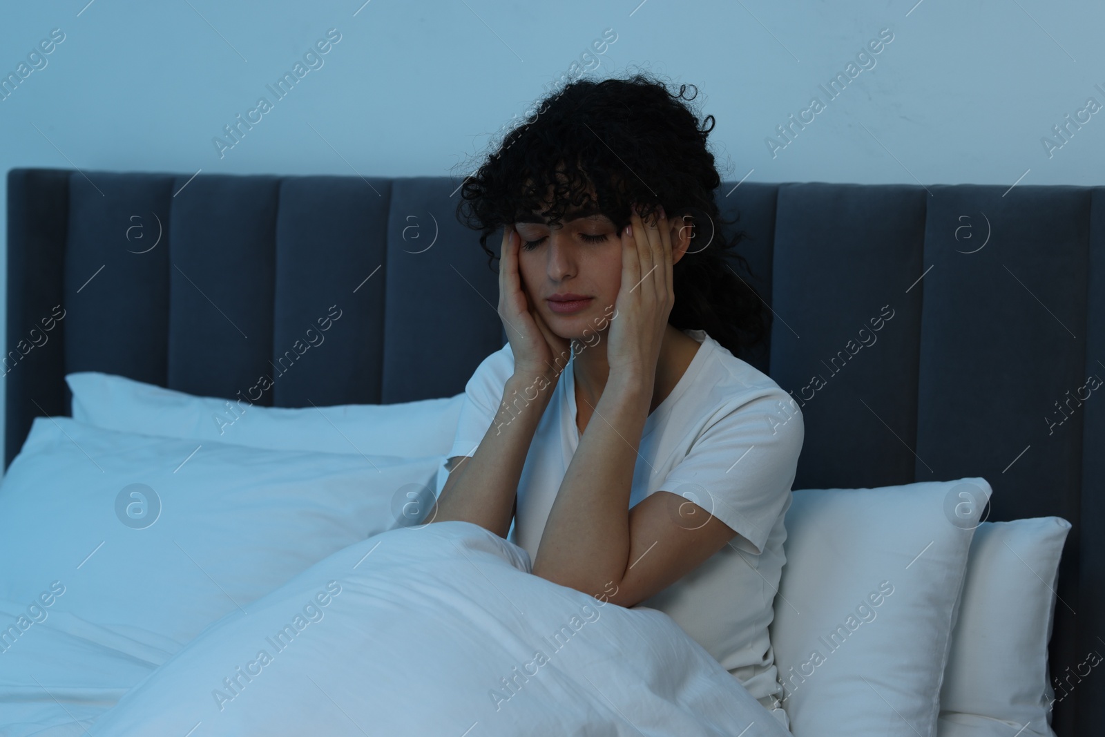 Photo of Young woman suffering from headache in bed at night