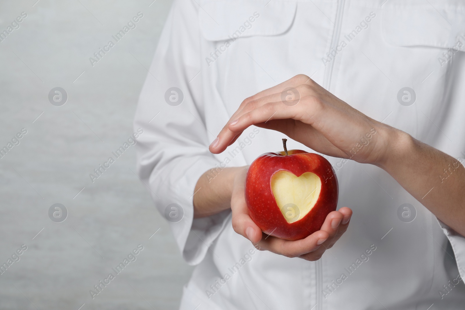 Photo of Woman holding apple with carved heart on light background, closeup