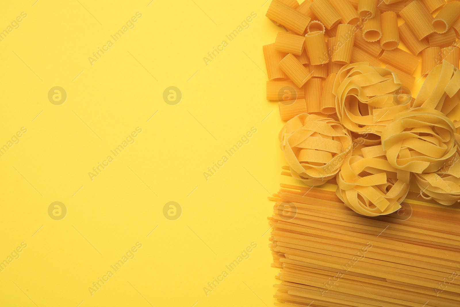 Photo of Different types of pasta on yellow background, flat lay. Space for text