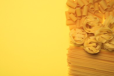 Different types of pasta on yellow background, flat lay. Space for text