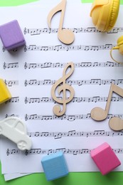 Photo of Wooden notes, music sheets and toys on light green background, top view. Baby song concept