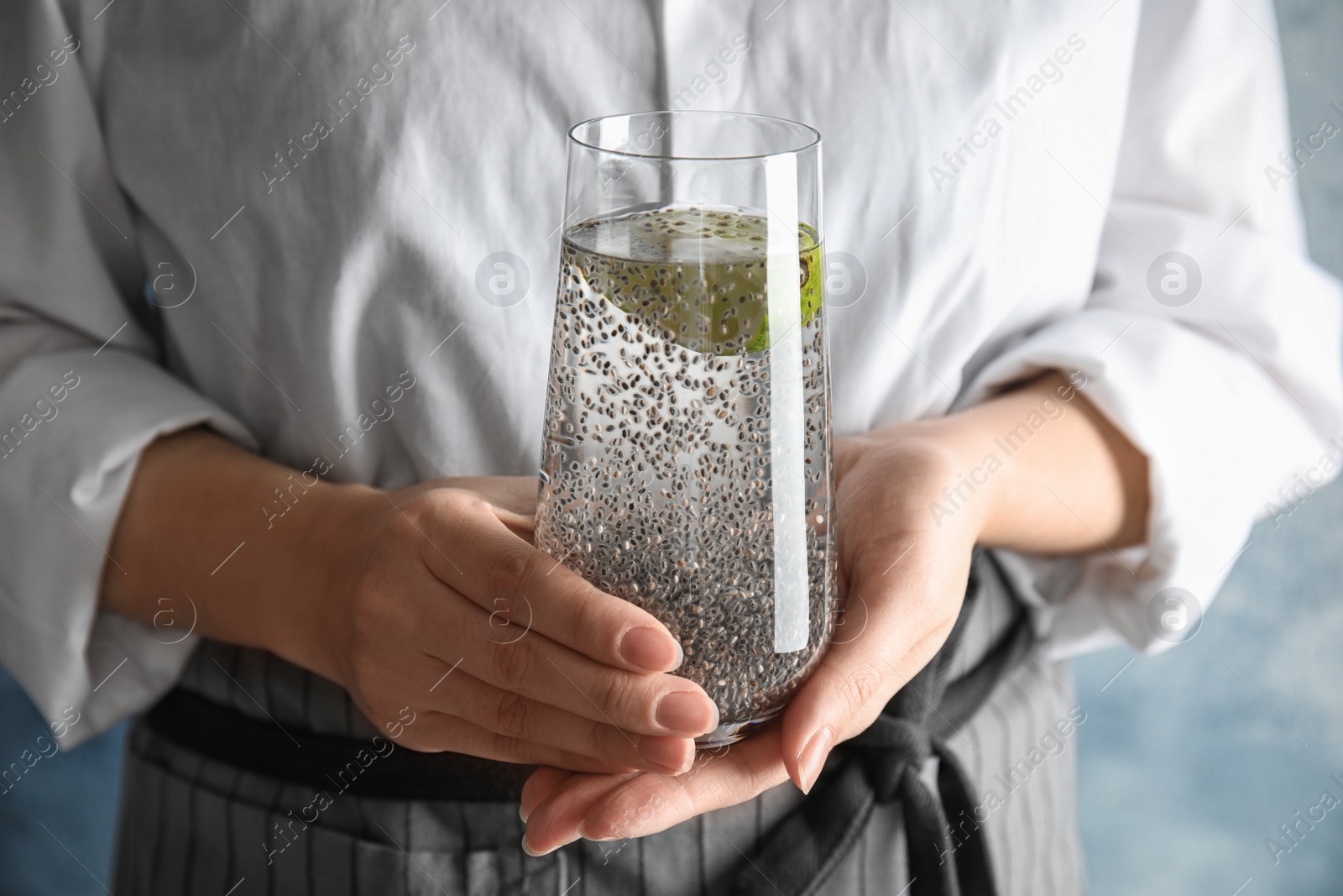 Photo of Woman holding glass of water with chia seeds on color background, closeup
