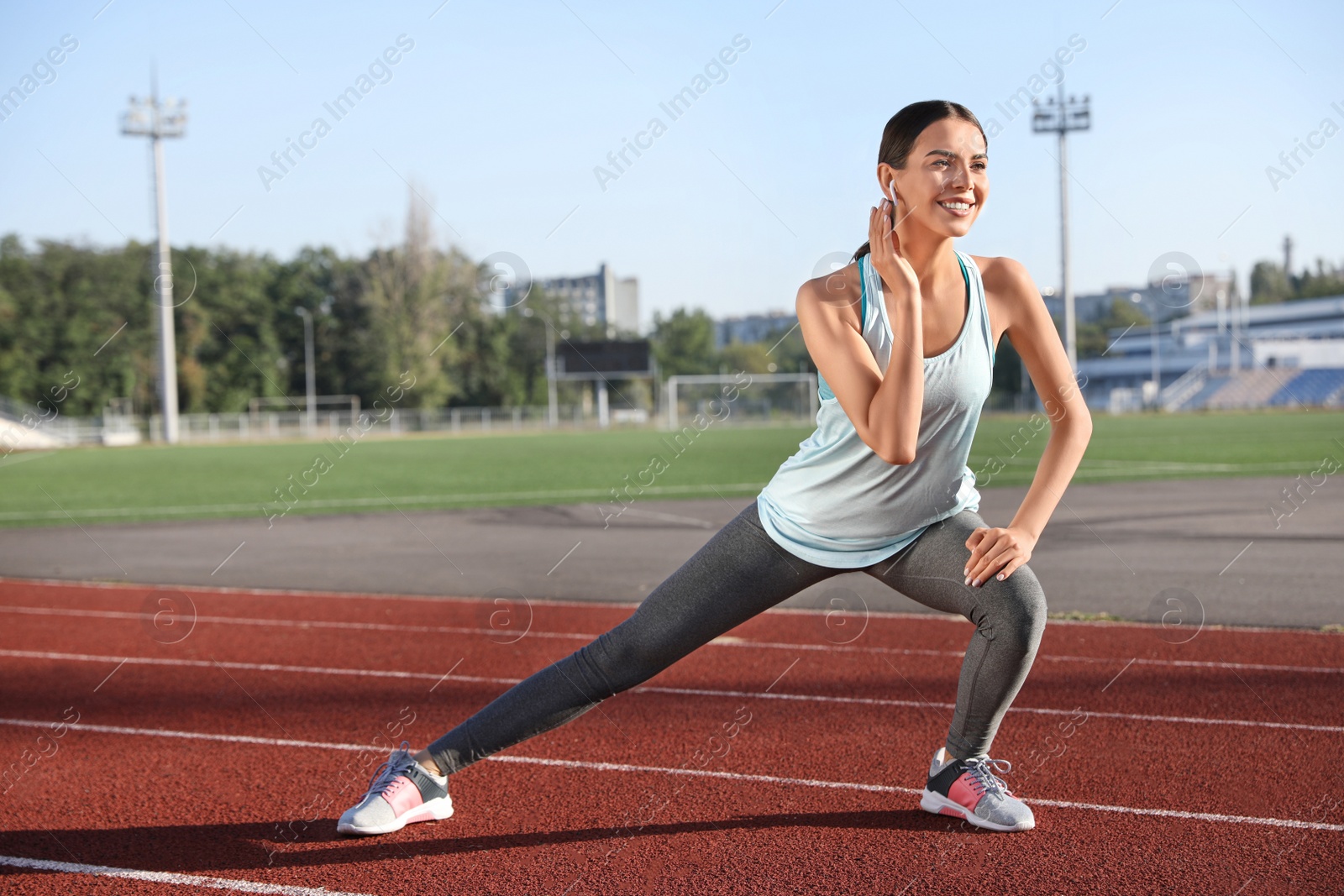 Photo of Young sportswoman with wireless earphones stretching at stadium