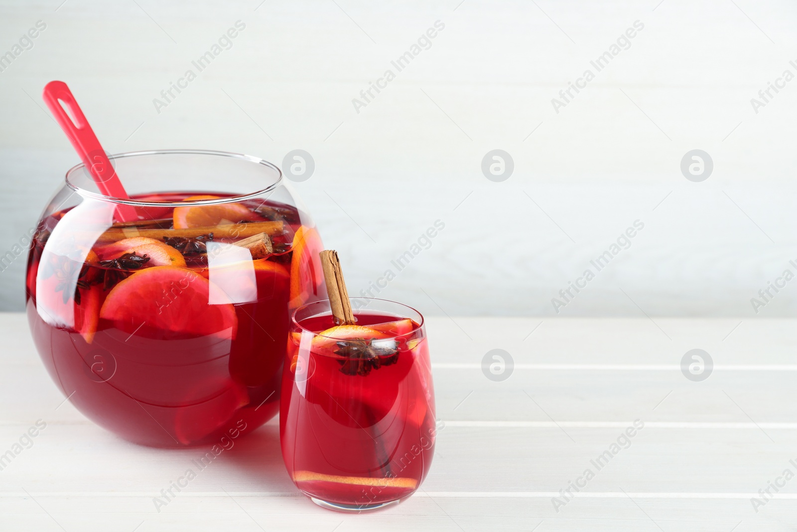 Photo of Glass and bowl of delicious aromatic punch drink on white wooden table. Space for text