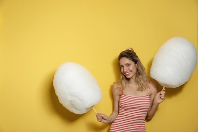 Portrait of pretty young woman with cotton candy on yellow background