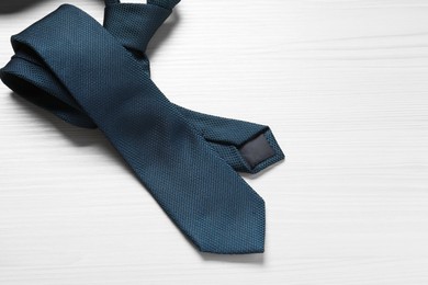 Photo of One blue necktie on white wooden table, top view. Space for text