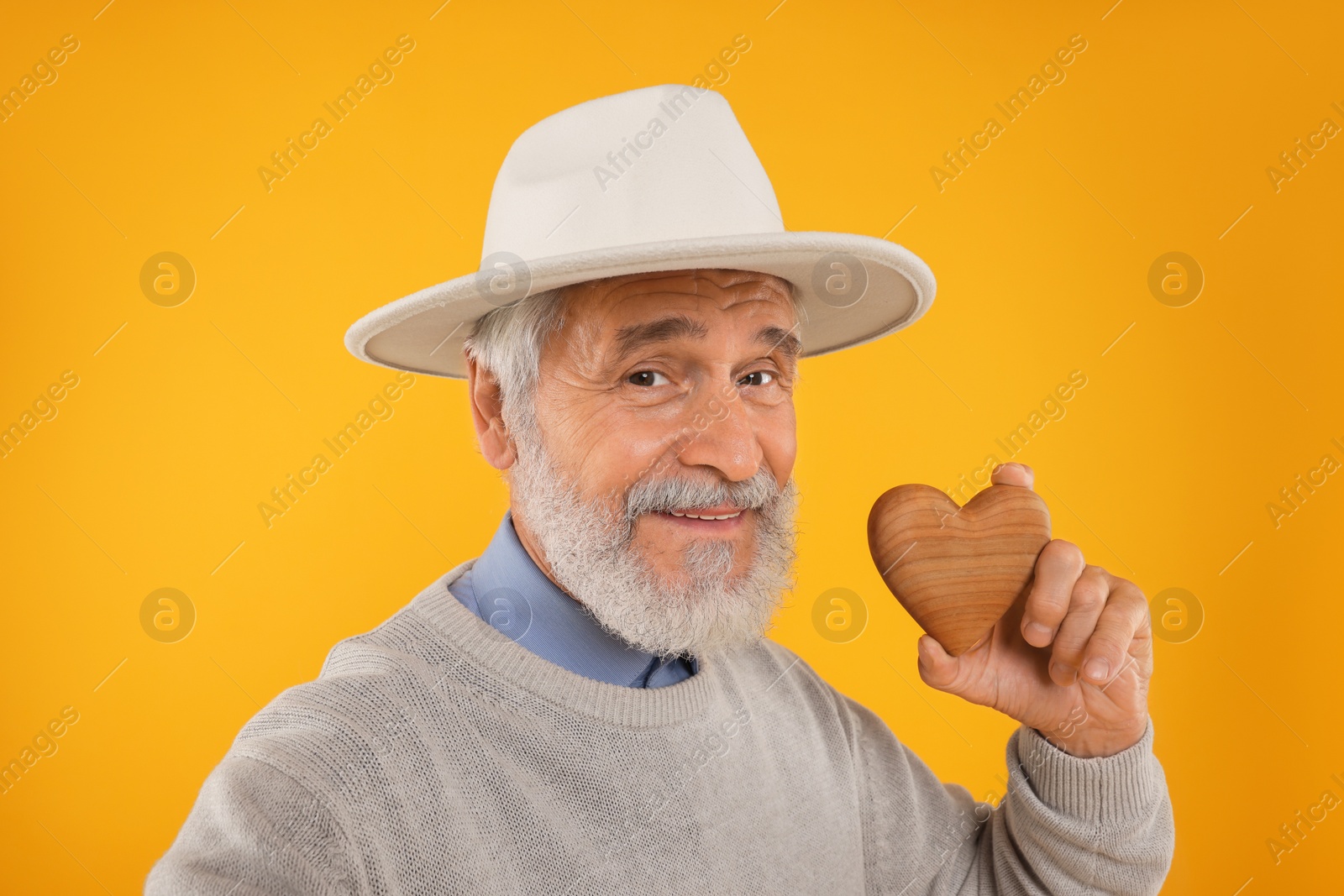 Photo of Senior man with wooden heart on yellow background
